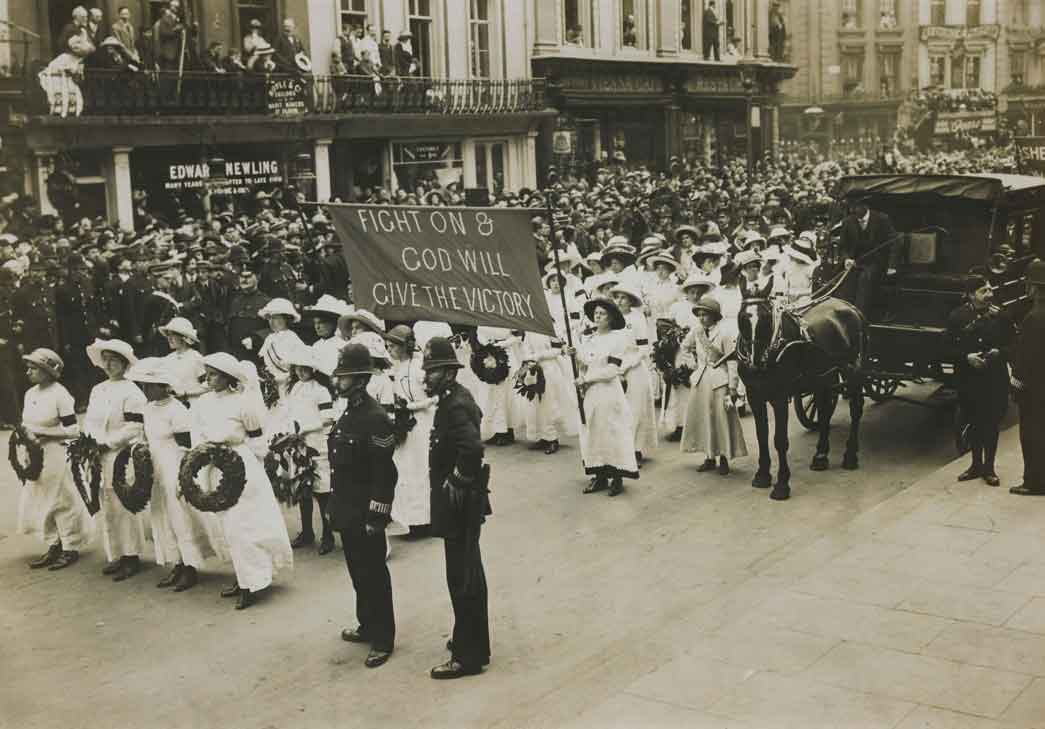 The funeral of Emily Wilding Davison, 14 June 1913. The image depicts one of the banners carriers in the procession bearing the defiant message 'Fight on & God will give the Victory' This banner in purple fabric preceded the long sections of London members of the Women's Social and Political Union. Ahead of the banner are Suffragettes carrying laurel wreaths. Suffragettes taking part in the procession were required to wear either white, purple, scarlet or black according to their role and position in the procession. As white succeeded purple and scarlet black the the resulting spectacular effect resembled, as noted the Manchester Guardian, 'the long unfurling of a military banner'. 