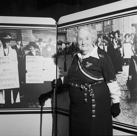 Former suffragette, Connie Lewcock. A government exhibition was staged inside Westminster Hall to mark the 50th anniversary of women's right to vote. Connie Lewcock O.B.E, an 84-year-old former suffragette from Newcastle, attended the private view, she is wearing some original suffragette movement insignia. Lewcock had helped to set fire to Esh Winning railway station in the name of suffrage. The exhibition, which included material from the Museum of London, opened with speeches from Prime Minister James Callahan, opposition leader Margaret Thatcher and Liberal Dame Margaret Corbett-Ashby.

