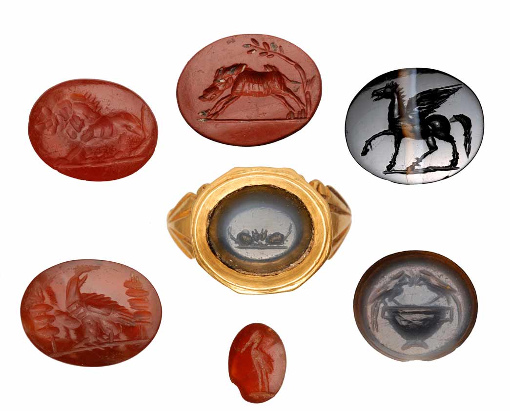 Selection of Roman intaglios. This group of roman intaglios showcases a variety of decorative motifs including animals, clasped hands and birds. Some of these intaglios were used as decoration for finger rings. The engravings on them are varied among them there are representations of animals, like the lion on the top left which could represent the sign of the zodiac Leo or be a symbol of strength worn to ward off the evil eye. In this instance, however, the lion more likely symbolises the devouring power of death. The intaglio on the centre left depicts a military eagle set between two legionary standards. The other engravings show a pair of clasped hands, the winged God Pegasus, two mice and parrots.
