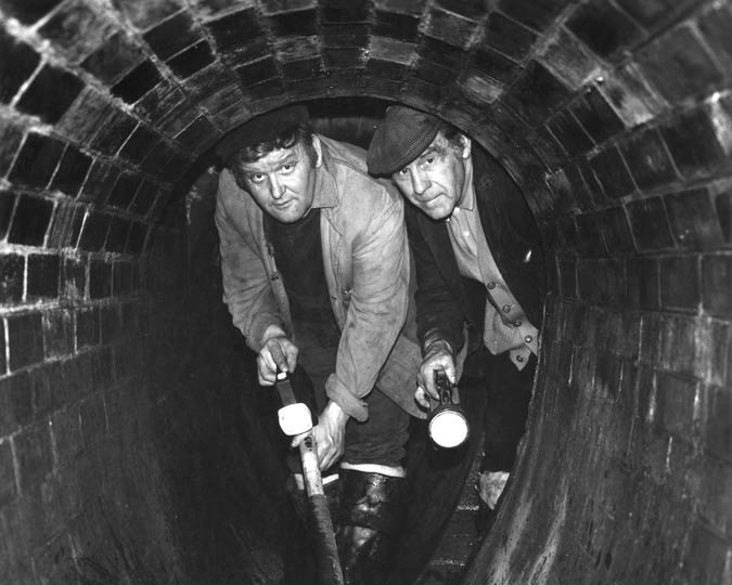 Two men in a Victorian brick-lined sewer photographed in the 1960s.