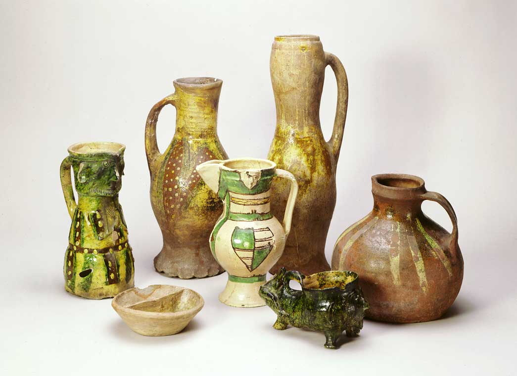 Selection of various types of medieval pottery. The museum of London's collection of medieval pottery is unique. This group of pottery, all found in London, is a small selection of a range of ordinary kitchen and tableware available to Londoners in the late 13th and early 14th centuries. The tall jars at the back come from kilns close to the medieval city. The small condiment dish, the drinking horn on the foreground and the conical jug with the human face (left) were all made in Kingston-upon-Thames, Surrey. The jug with stripped decoration (right) was made at Mill Green, near Chelmsford in Essex. The jug in the centre, of fine white clay with painted shields, is from the region of Saintes in Western France and probably came to London with the wine trade from Bordeaux.
