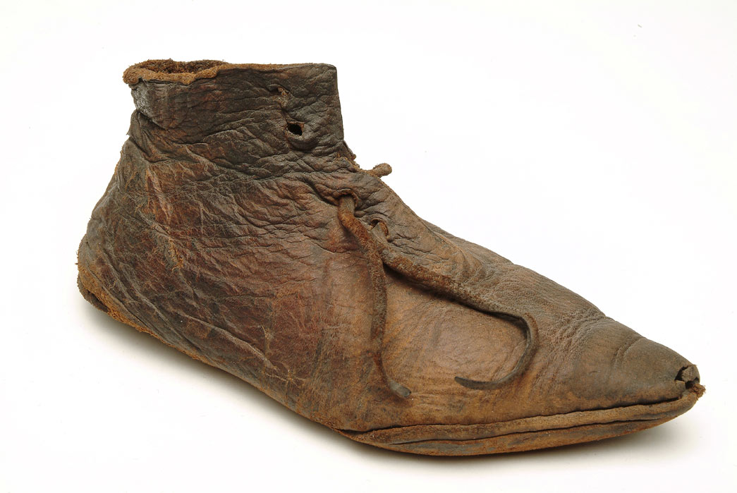 Small leather shoe with a pointed toe and leather laces. The upper part of the shoe is made from one single part of leather. This shoe is lightweight, flexible with a thin sole. During the medieval period children's shoes were similar to those worn by adolescents and adults. The only exceptions were the exaggerated, long, pointed 'poulaines', which were only worn by adults. This child's ankle-shoe dates to the late 1300s. It is fastened at the front with a leather thong. It was found at Baynard's Castle Dock, near Blackfriars, London.
