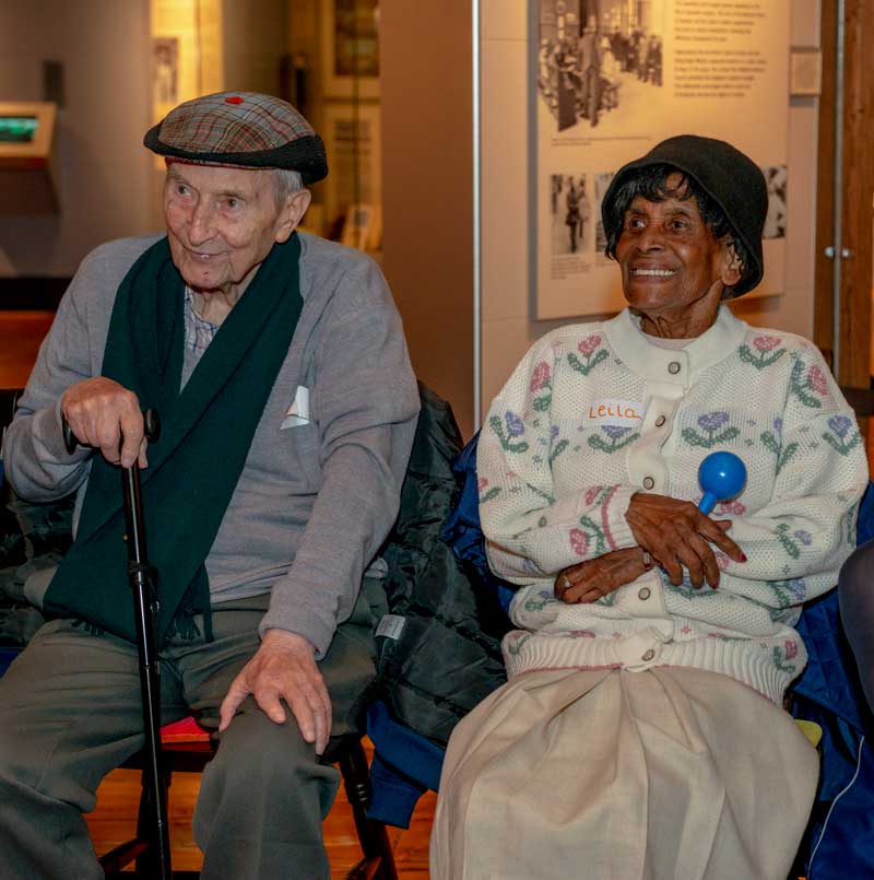 Two smiling visitors sit next to each other within the Museum of London Docklands' galleries.
