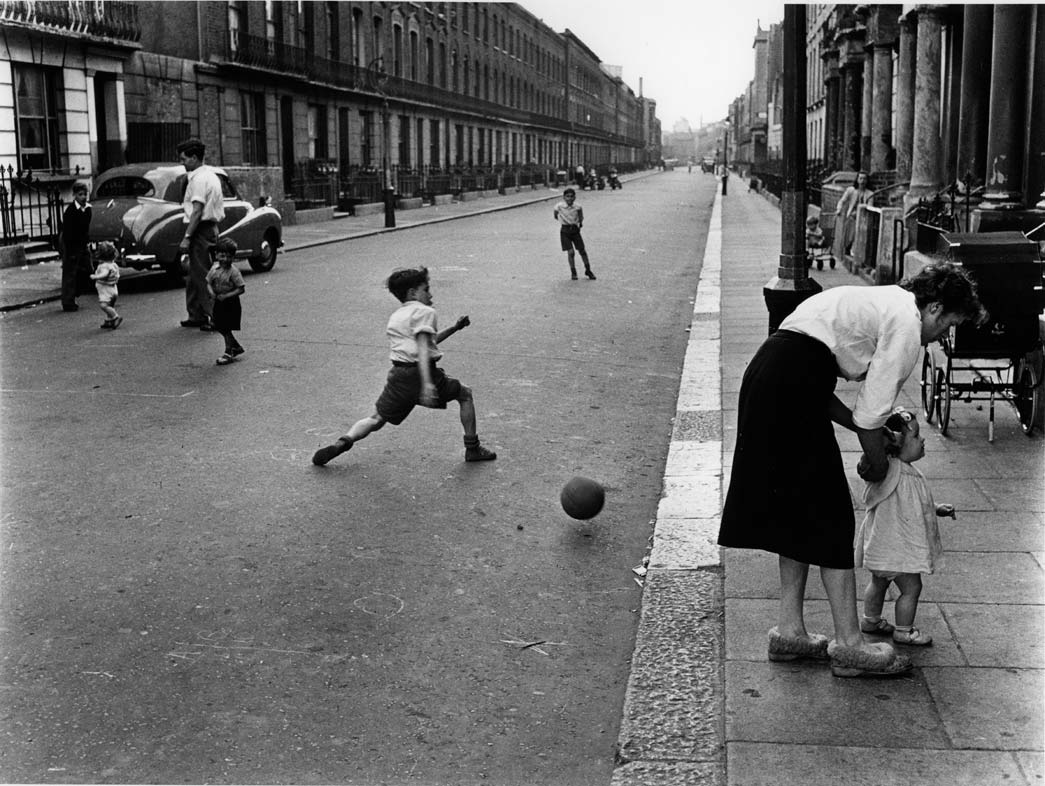 Southam Street, North Kensington, with boys playing football, 1956. Before the replacement of terraced houses by tower block estates and the rapid growth of car ownership, streets like this were communal spaces and playgrounds for children and adults alike. 

