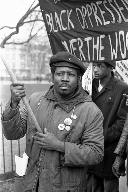 This photograph by Neil Kenlock, the official photographer to the British Black Panther movement, depicts demonstrators during a Black Panther rally. Several men are seen walking with badges and banners along a street in London, protesting against 'BLACK OPPRESSION'.