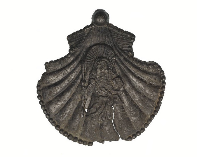 St James of Santiago de Compostela: Pilgrim badge from the shrine of St James in Santiago de Compostela in north-west Spain. This badge is in the shape of a scallop shell. In the centre of the shell is a standing figure of St James dressed as a pilgrim with a cloak, a satchel and holding a staff. 