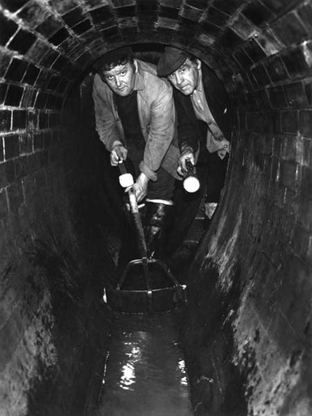 Sewer cleaners, Sam Luck (left) and Robert Attwood, beneath Lower Thames Street in a 19th century brick sewer, 1974. The men had worked in the sewers for 18 and 23 years respectively and both had previously been dustmen.

