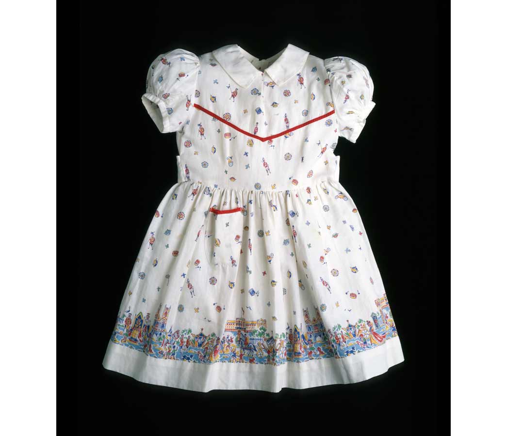 A child's dress made to be worn by the donor, Helen Clark, in celebration of the coronation of Queen Elizabeth II in 1953. The pattern of the dress's cotton fabric is composed of cartoon images of events of the coronation, including the queen on a throne, Buckingham Palace, coach processions, royal guards, and crowds of cheering spectators. The dress has small puffed sleeves, a Peter Pan collar on a round neck, gathered skirt, and pocket on the left side.

