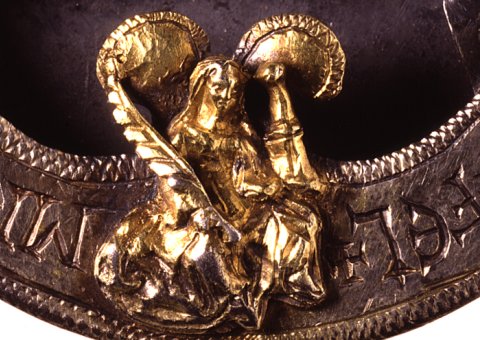 Close-up photograph of the small gold-coloured model of a seated woman which forms the central decoration on the chape