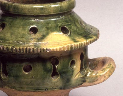Photograph of green glazed pot with a tall base and two loop handles. The base is hollow to contain a burning coal, and the top is open, to hold the herbs. There are small holes in the sides to allow the fumes to spread.