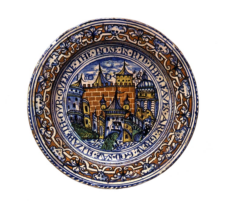 Photograph of a plate decorated in blue, brown and yellow designs. The rim has an interlocking design of faces, leaves and curling lines. The centre has a picture showing the city walls and gate. Around the picture is an inscription in English.