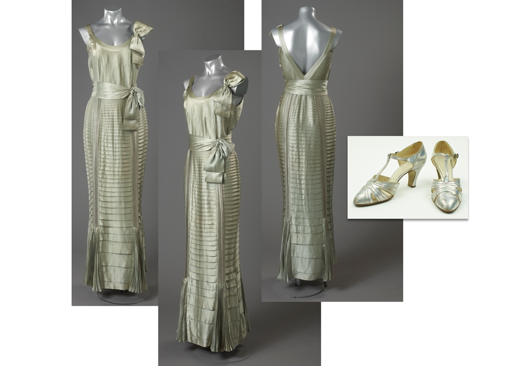 Ingeniously pleated evening dress in fluid silk by Norman Hartnell. The silver evening sandals by Lilley & Skinner feature the fashionable T-bar (ID nos: 73.139; 76.7/3)