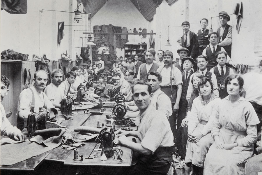 black and white photo of men and women in a garment factory sitting and standing around a table with sewing machines
