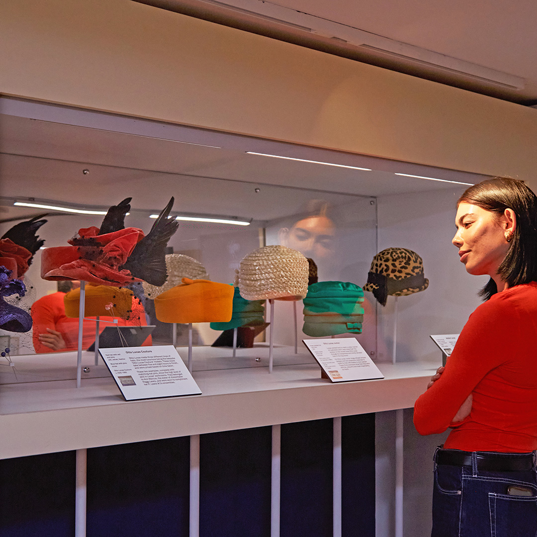 A woman looking at the hats on display in Fashion City at Museum of London Docklands