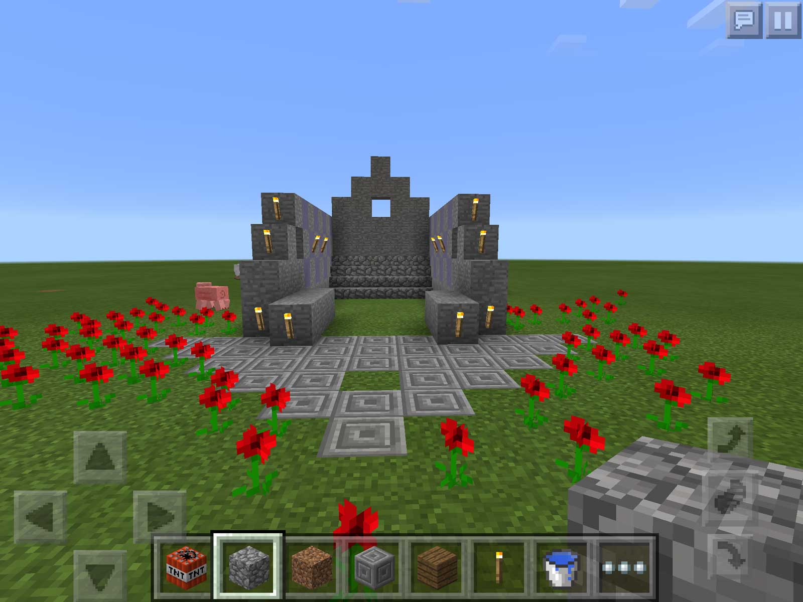 Screenshot of a Minecraft game in progress, where a stone arch has been built surrounded by red flowers.