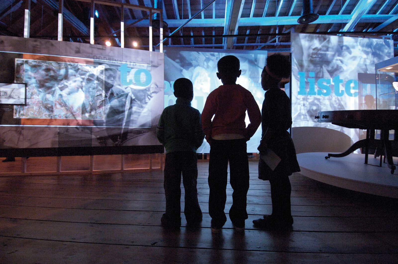 Three children watch a sound and light show in the Sugar and Slavery gallery at the Museum of London Docklands.