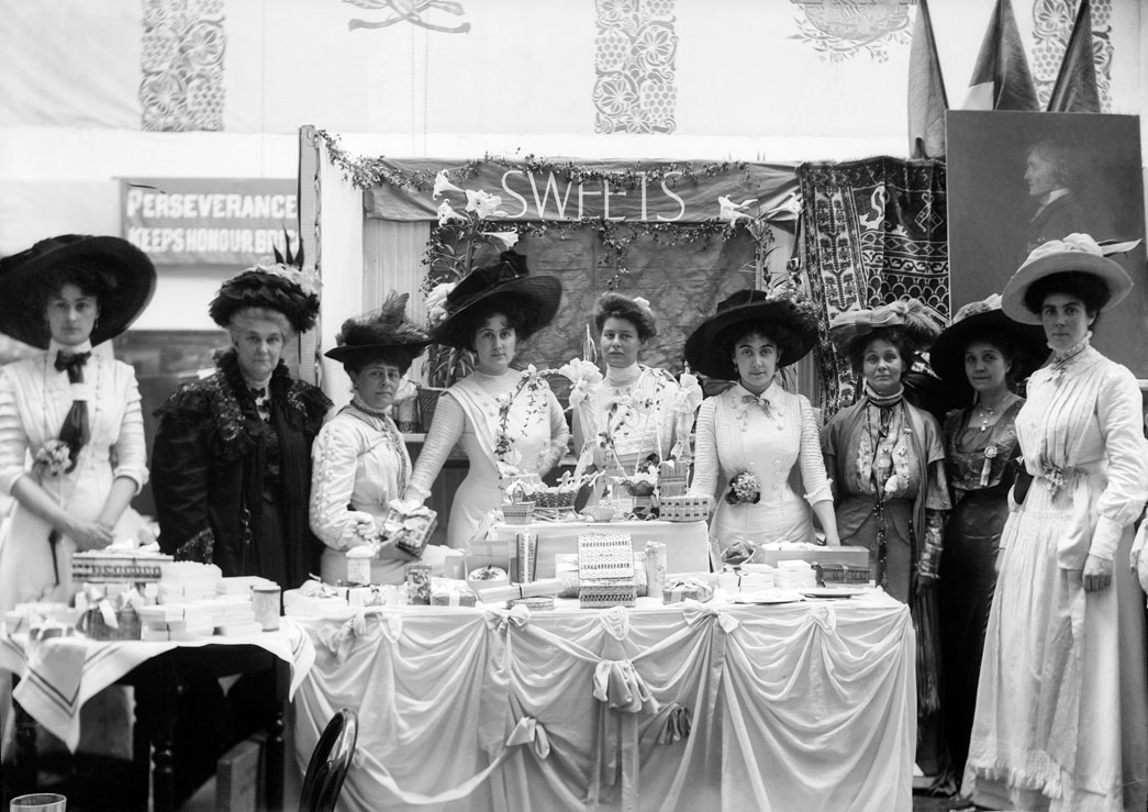 Suffragette exhibition stand, May 1909. More than 50 stalls were set up at The Women's Exhibition held at Prince's Skating Rink, Knightsbridge, on 13-26 May 1909. The various stalls were decorated by the stall-holders to include the Women's Social and Political Union colours of purple, green and white. Sale proceeds from the exhibition went into the union's suffrage campaign fund.
