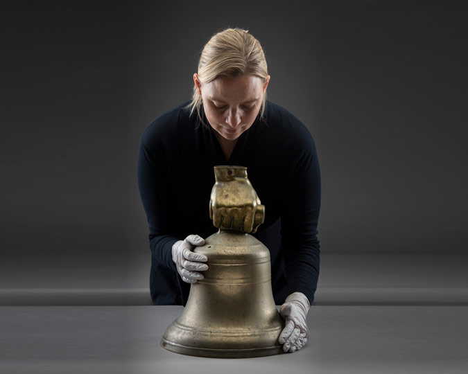 A brass bell from Holloway prison being held by a curator