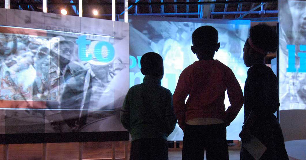 3 children standing with their backs to the camera look at a display in the London, Sugar and Slavery gallery.
