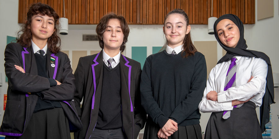Four secondary school students in school uniforms standing and smiling