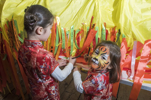 Two children in Chinese dress, one of whom has her face painted like a tiger.