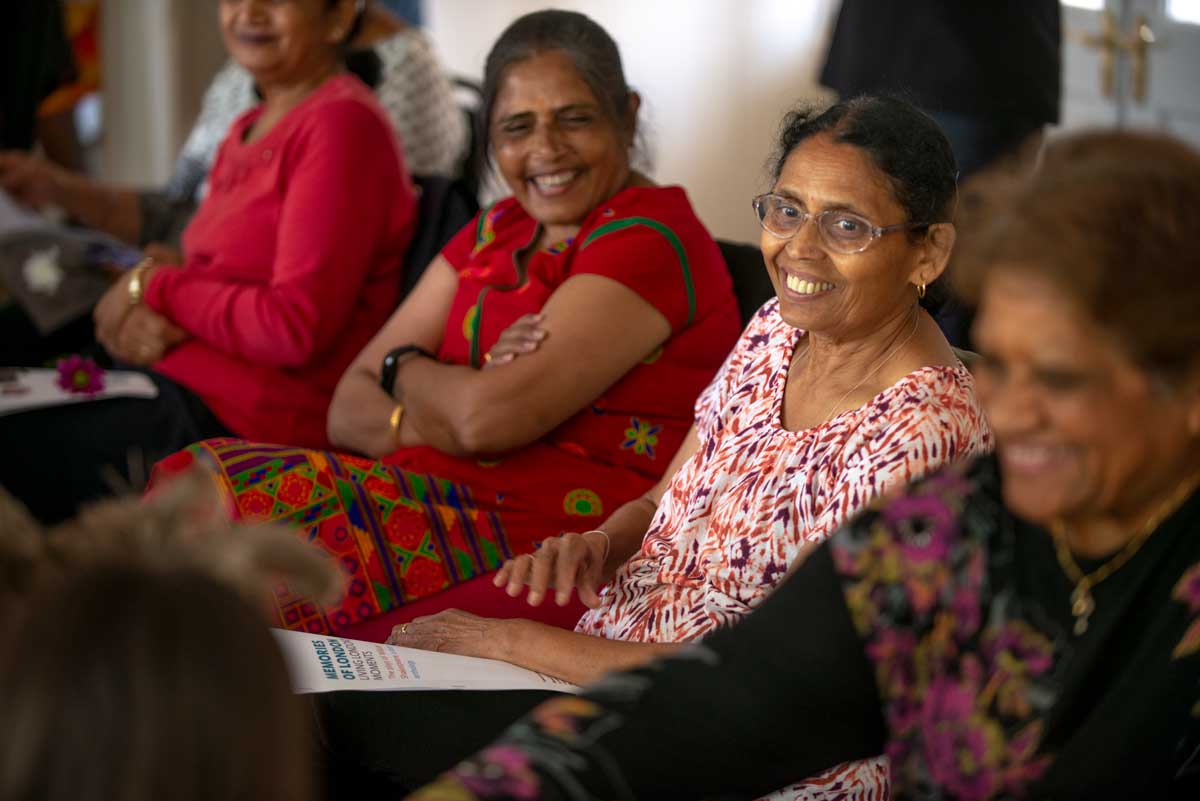 Four women smile while sitting in a line at a dementia outreach event.