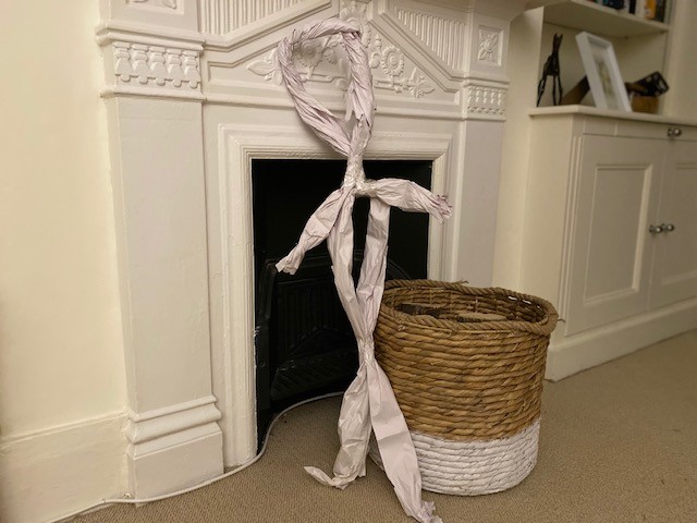 A paper puppet just under a metre tall stands beside a fireplace in someone's house.