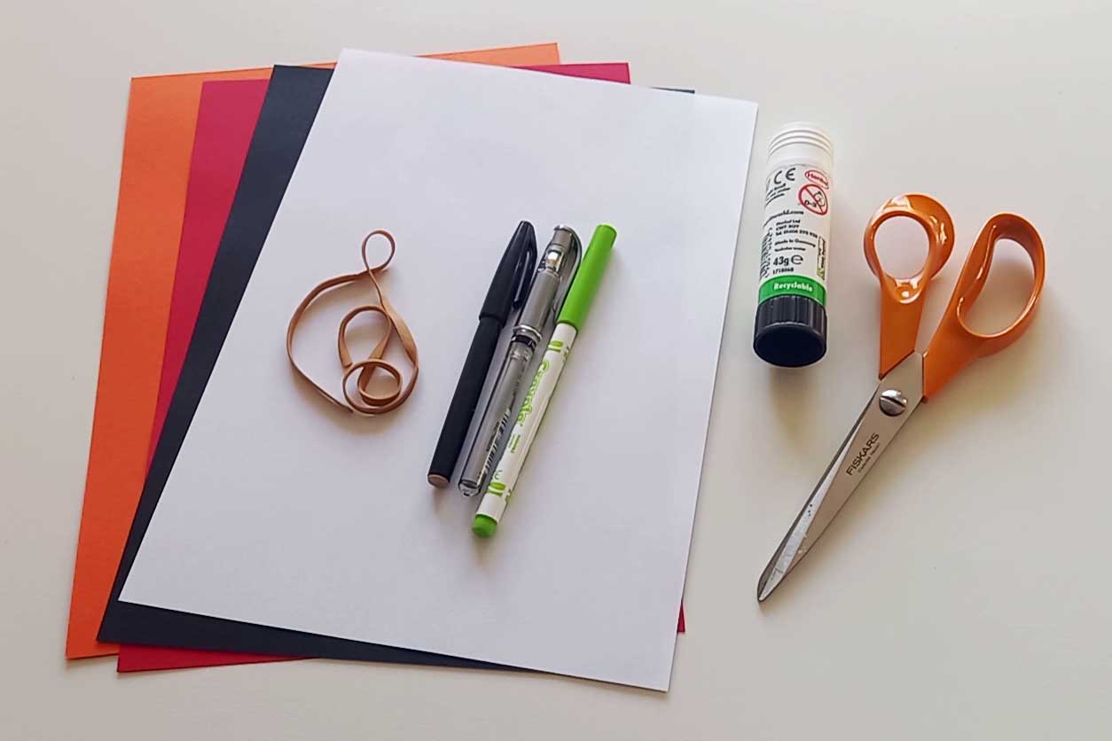 A pair of scissors, a glue stick, three pens, a rubber band and four sheets of coloured paper.