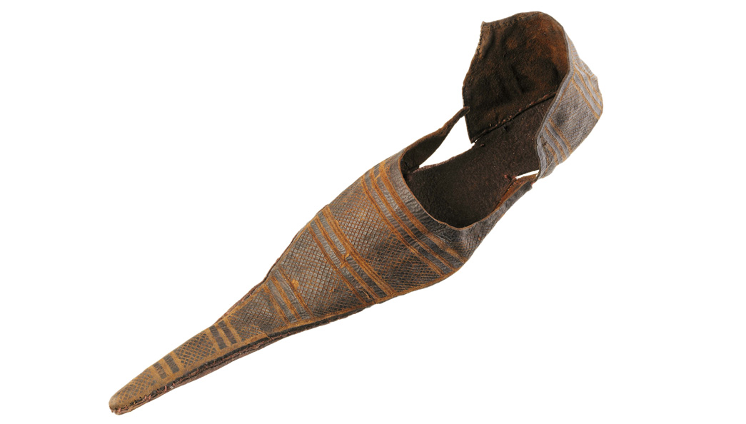 Pointed medieval shoe known as a 'poulaine'. It has a latchet fastening (a leather strap split into two at the end, which goes through a pair of holes).