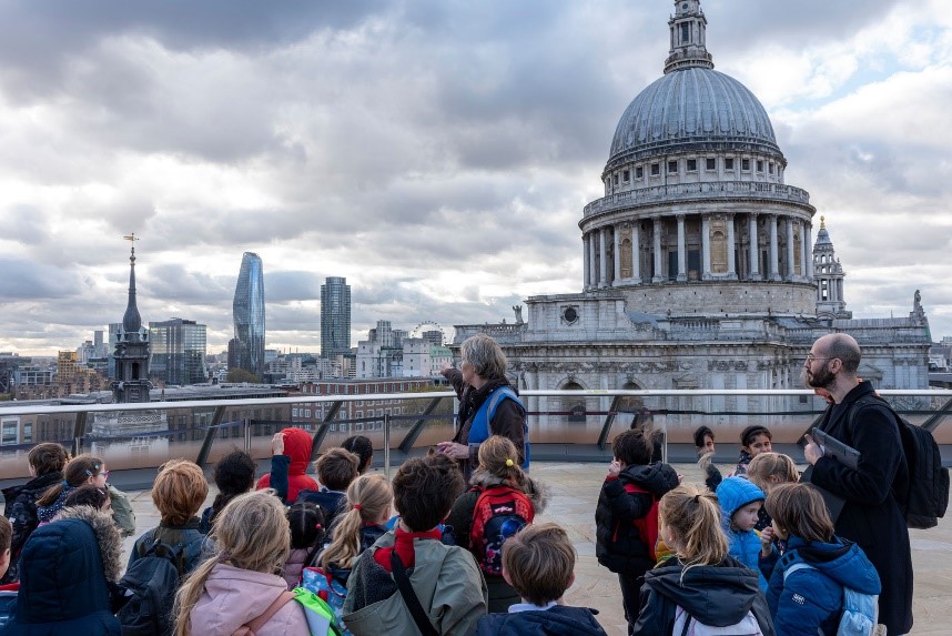 A group of school children and two adults on a viewing platform looking at St Paul's Cathedral