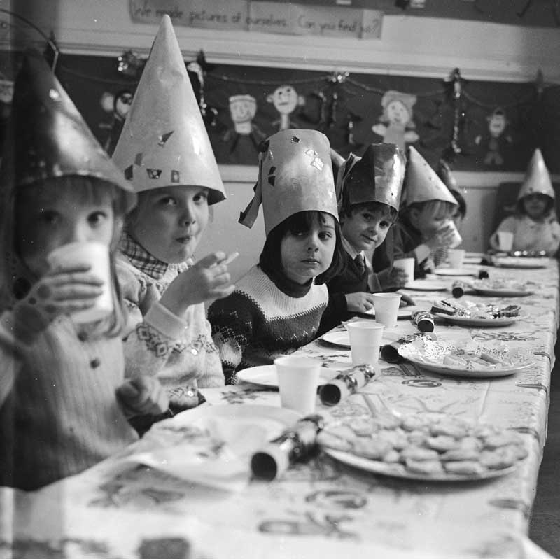 Photo of children sat at a table wearing party hats that they have made and decorated themselves.