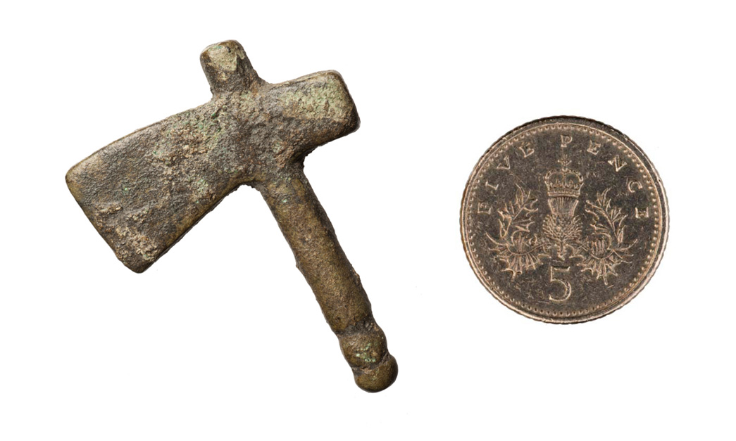 A miniature Roman model of an axe, photographed next to a 5 pence coin for scale.