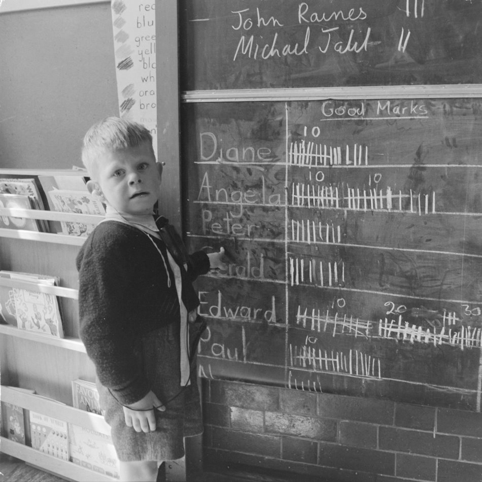 A kid at Ackmar Road School for Deaf Children
This little boy – presumably Gerald or Peter – points proudly at his ‘Good Marks’ tally in class, 1958. (ID no.: HG1827/08, ©Henry Grant Collection/Museum of London)
