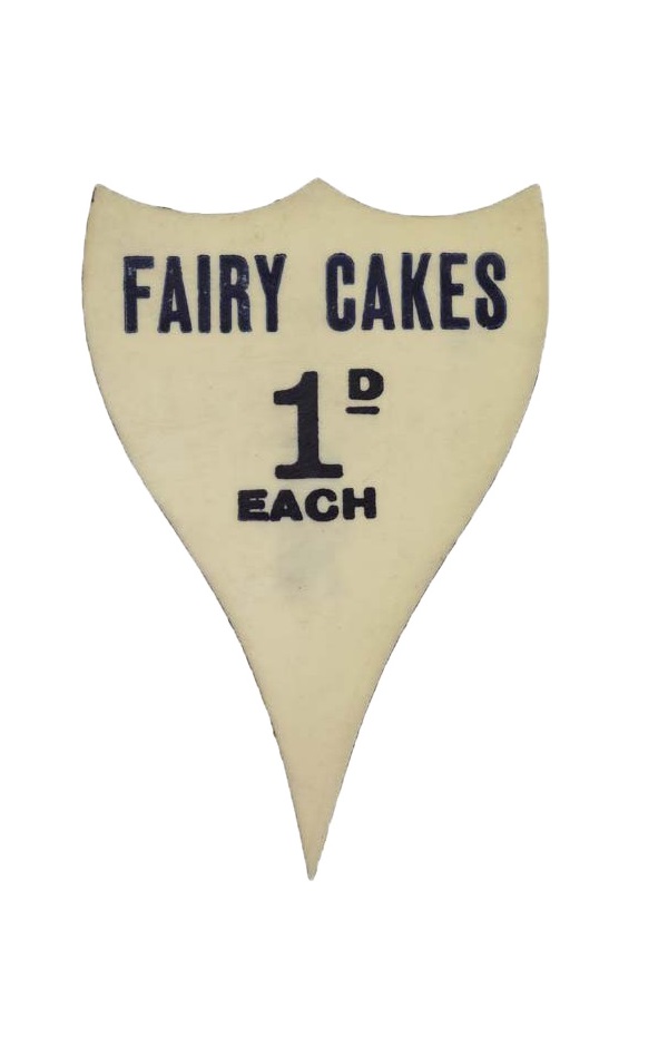 Plastic price ticket marked 'FAIRY CAKES 1d EACH', from Stanley Bakery 219 Eversholt Street, NW. The bakery, which closed in 1966, baked bread, cake and buns in the basement and sold them from a counter on the ground floor.