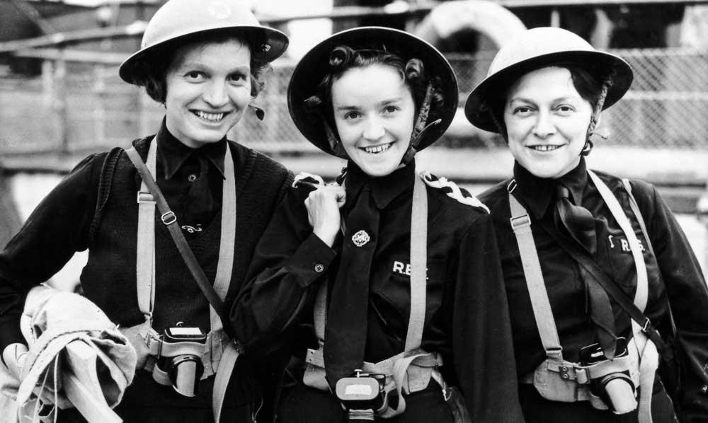 Three smiling women in uniform wearing metal helmets.