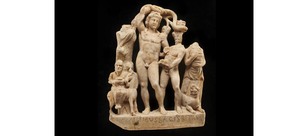 A marble sculpture from the Temple of Mithras in London depicting Bacchus and his followers. Bacchus was the Roman god of wine. Above his head is a vine branch. (ID no.: 18496)