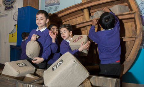 school children playing with cargo box props on a replica boat
