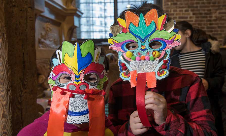 Two children hold brightly coloured decorated masks in front of their faces.