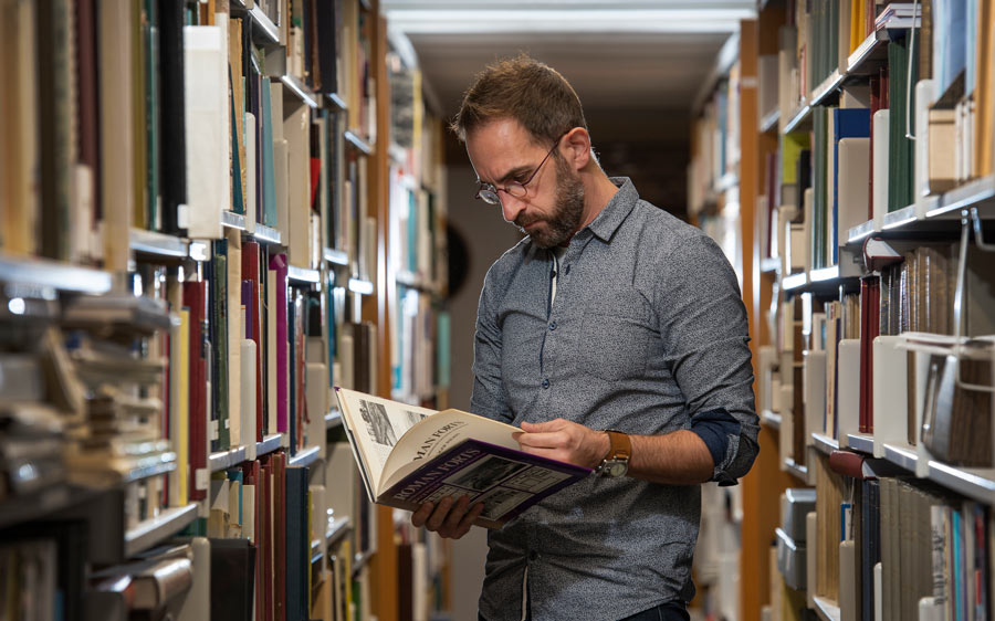 A man reading a book in the library stacks.