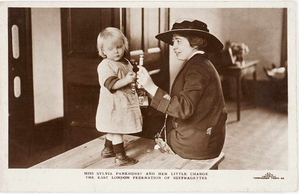 Postcard with a photograph of Sylvia Pankhurst (1882-1960) playing with a child who is standing on a table in the Mother's Arms, 1913–16. (ID no.: 50.82/871a)