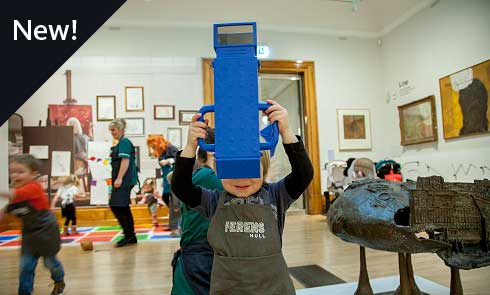 A photograph of a young child holding a big, blue, periscope in a busy gallery space.